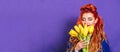 Beautiful girl with red hair stands on a purple background and holds a bouquet of yellow tulips. Concept of holiday - March 8, Royalty Free Stock Photo