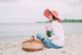 Beautiful girl in a red hat with picnic basket at the summer waterfront.