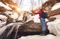 Girl stands arms up in front of the winter waterfall and orange sun