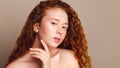 Beautiful girl with red long curly hair and brown eyes without makeup looks at the camera. Studio shot on a beige background Royalty Free Stock Photo