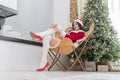 Beautiful girl in red Santa suit sits on the floor near fireplace and Christmas tree with a gift box. Magical Christmas night in Royalty Free Stock Photo