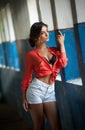 Beautiful girl with red shirt and white shorts posing in old hall with columns blue painted. Attractive long hair brunette Royalty Free Stock Photo