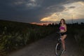 Beautiful girl riding bike at fields at sunset