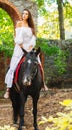 A beautiful girl riding a horse looks away. In the park. Side view. Royalty Free Stock Photo