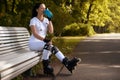 Beautiful girl on roller skates in park sits on bench and drinks water
