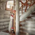 A beautiful girl in a Russian costume is standing on a wooden staircase