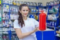 Beautiful girl saleswoman offers an extinguisher in an auto parts store. Compliance with travel safety regulations