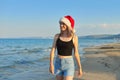 Beautiful girl in Santa hat walking along beach. Christmas and New Year holidays Royalty Free Stock Photo