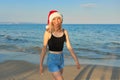 Beautiful girl in Santa hat walking along beach. Christmas and New Year holidays Royalty Free Stock Photo