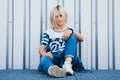 Beautiful girl with short white hair dressed in jeans in urban style sits on the background of a white wall. A look at the camera Royalty Free Stock Photo