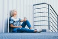 Beautiful girl with short white hair dressed in jeans in urban style sits on the background of a white wall. Place for text Royalty Free Stock Photo