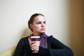 A beautiful girl sits against the yellow wall, holds a cardboard cup of coffee and looks to the side