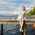 A beautiful girl sits alone on a river pier under a clear sun and looks at the water. The wind develops her blond hair curls. Royalty Free Stock Photo