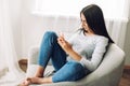 A beautiful girl sits in a chair with a phone in her hands, writes messages, makes purchases, views and publishes posts Royalty Free Stock Photo