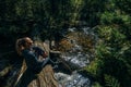 Beautiful girl sits on log and chilling after travel. Woman traveler in summer passes on wooden bridge in background of Royalty Free Stock Photo