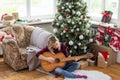 beautiful girl sits near the Christmas tree decorated with balls and light and playing the guitar and singing. Young Royalty Free Stock Photo