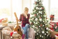 beautiful girl sits near the Christmas tree decorated with balls and light and playing the guitar and singing. Young Royalty Free Stock Photo