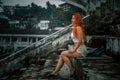 A beautiful girl sits in the stands of an abandoned stadium. It's a nasty day.