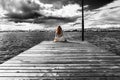 A beautiful girl is sitting alone on the river pier against the backdrop of thunder clouds and looks into the distance. Royalty Free Stock Photo