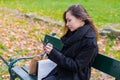 Beautiful girl sitting on a bench, woman with your phone writes a message on social networks, sunny autumn day in the Royalty Free Stock Photo