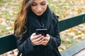 Beautiful girl sitting on a bench, woman with your phone writes a message on social networks, sunny autumn day in the Royalty Free Stock Photo