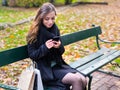 Beautiful girl sitting on a bench, woman with your phone writes a message on social networks, sunny autumn day in the park, woman Royalty Free Stock Photo