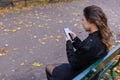 Beautiful girl sitting on a bench, woman with your phone writes a message on social networks, sunny autumn day in the park, woman Royalty Free Stock Photo