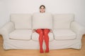 Beautiful girl is sitting on the couch covered with a pillow.