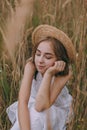 Beautiful girl sitting in a field. Attractive young woman in white bohemian dress with windy hair holding relaxing among leaves.