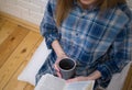 Beautiful girl is sitting on the floor in loft minimalist interior. Young woman in men`s checkered shirt is drinking coffee and Royalty Free Stock Photo