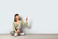 Beautiful girl sitting on floor and pointing at something against white background. Space for text Royalty Free Stock Photo