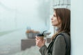 Beautiful girl sitting in foggy street holding coffe in hands and drinking through straw