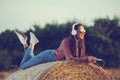 Beautiful girl sitting on a haystack, listening to music , enjoying sunset.