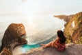 Beautiful girl sitting on a high rock and looking out to sea, rear view. Girl sits on the edge of cliff. The girl of the sea.