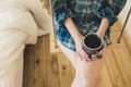 Beautiful girl is sitting on swing in loft minimalist interior. Young woman in men`s checkered shirt is drinking coffee. Cozy Royalty Free Stock Photo