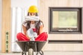 Beautiful girl sitting in a wheelbarrow inside the construction site with wearing overall and a hard hat, hiding face behind a Royalty Free Stock Photo