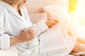 Young woman in white terry robe is drinking coffee and reading magazine or book in bedroom. Royalty Free Stock Photo