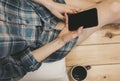 Beautiful girl is sitting on the wooden floor. Young woman in men`s checkered shirt is drinking coffee and searching in social Royalty Free Stock Photo