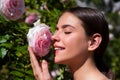 Beautiful girl smelling a rose flower in spring park. Young woman in flowering garden with roses. Beauty model with