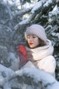 Beautiful girl among the snow-covered pines stands in a warm hat and mittens. Sunny winter day Royalty Free Stock Photo