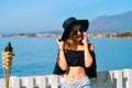 A beautiful girl speaks on the phone against the backdrop of the beach and ocean, sea. Woman in a big black hat and glasses on Royalty Free Stock Photo