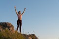 Beautiful girl in sportswear remains on top of a mountain and looks at the horizon with a rasied hands