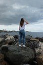 Beautiful girl standing on beach rocks looking to the sea Royalty Free Stock Photo