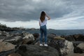 Beautiful girl standing on beach rocks looking to the sea