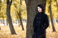 Beautiful girl standing near tree in autumn city park, yellow leaves on background, fall season, dressed in black coat Royalty Free Stock Photo