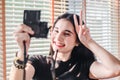 Beautiful girl standing in the room and taking selfie video for fashion blog. Woman holding compact camera in her hand and taking Royalty Free Stock Photo