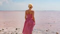 A beautiful girl stands back against a pink salt lake in a red dress in a caged on the censor`s frame Royalty Free Stock Photo