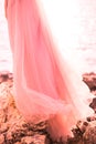 Beautiful girl stands sideways in a pink dress of tulle on the nature of the sea with rocks. The concept of fashion colors 2019 Royalty Free Stock Photo