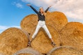 Beautiful girl on straw bales. Young woman in white jeans and black shirt jumping on a haystack. Female portrait in Royalty Free Stock Photo