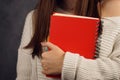 Beautiful girl student in a sweater with a red notebook on a dark backgroundred notebook in the hands of a girl